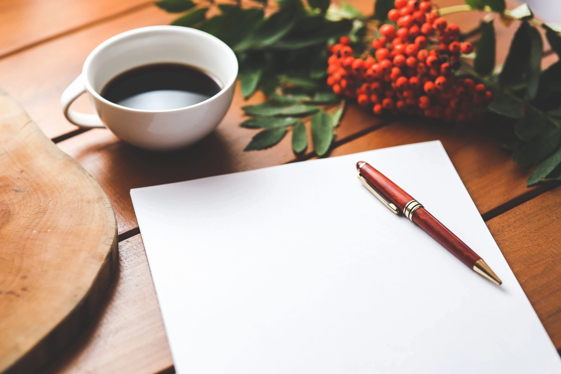 Blank paper with pen and coffee on a wooden desk